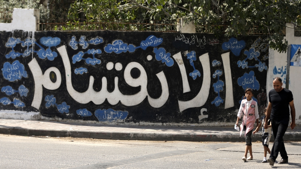 A Palestinian man and children walk past graffiti reading “division” in Arabic, in Gaza City, in 2017 [AFP]
