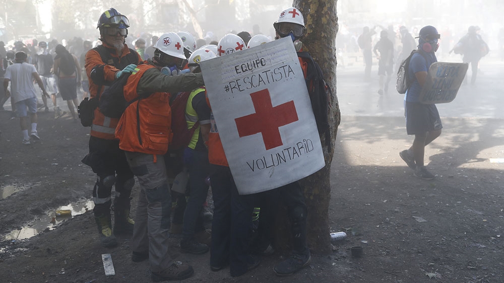 Medical personnel shield together to protect themselves from tear gas and rubber bullets during a protest against Chile’s government in Santiago