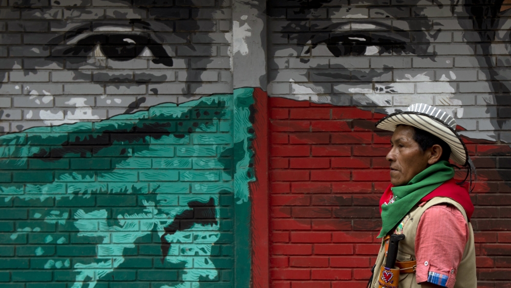 An Indigenous Guard from the Nasa tribe walks by a mural in Toribio, department of Cauca, Colombia