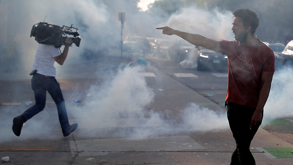 A protester argues with law enforcement officers as a reporter runs away from tear gas during a demonstration against the killing of George Floyd